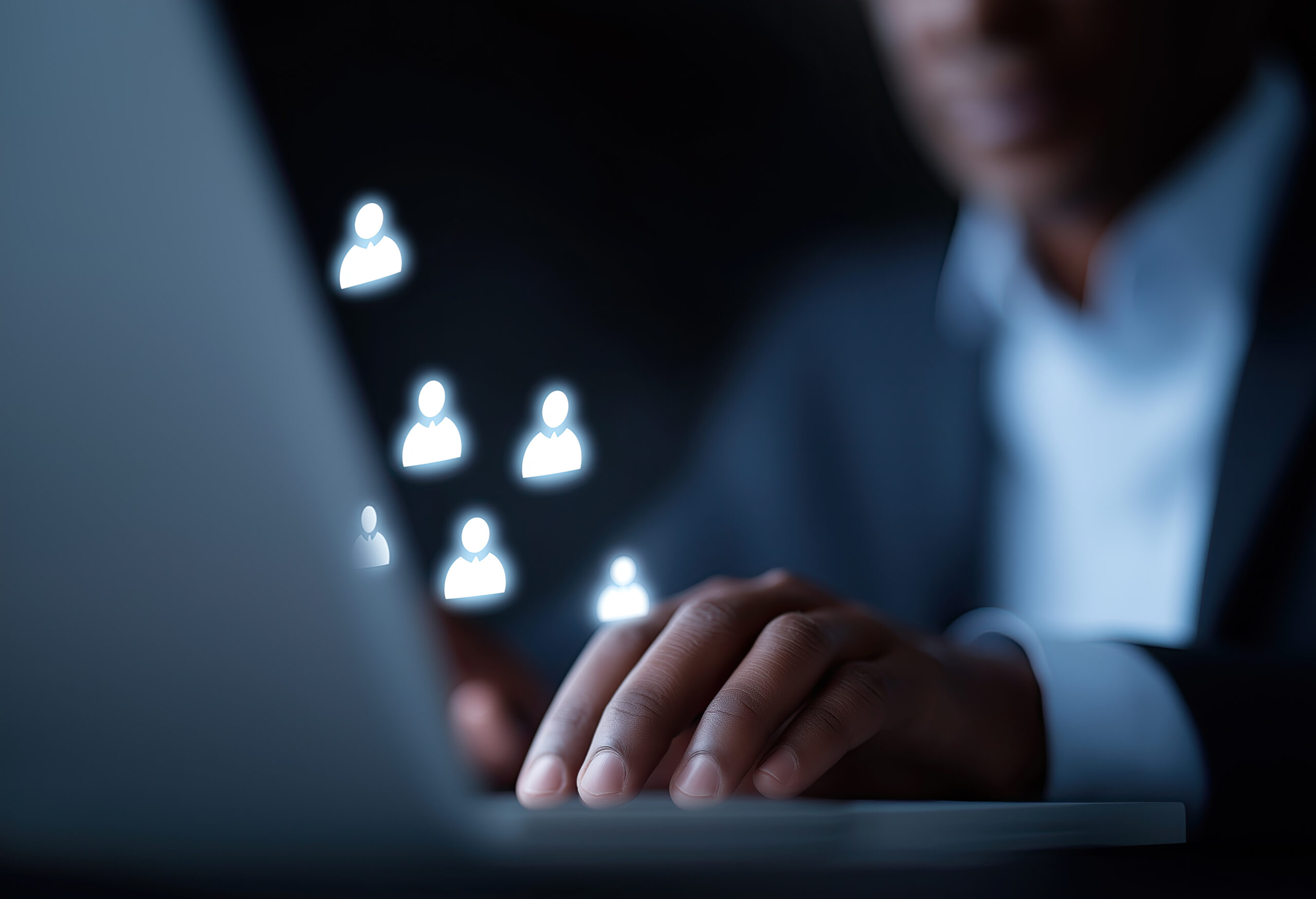 Businessperson types while glowing user icons float nearby Hands typing on a keyboard with glowing user icons floating above, symbolizing online teamwork.