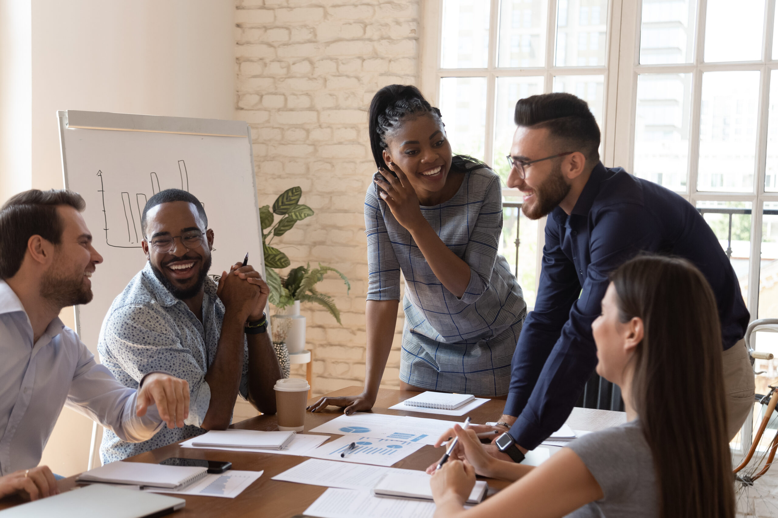 Happy friendly multiracial team laughing working together at corporate briefing Group of colleagues around a table in a bright office, smiling and discussing charts and documents.